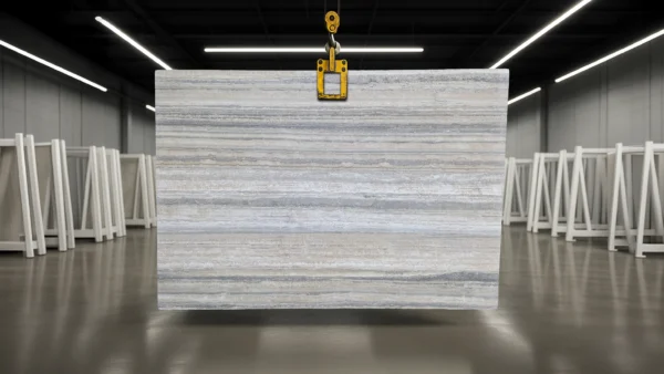 Large gray striped stone slab suspended by a yellow lifting clamp in an industrial warehouse.